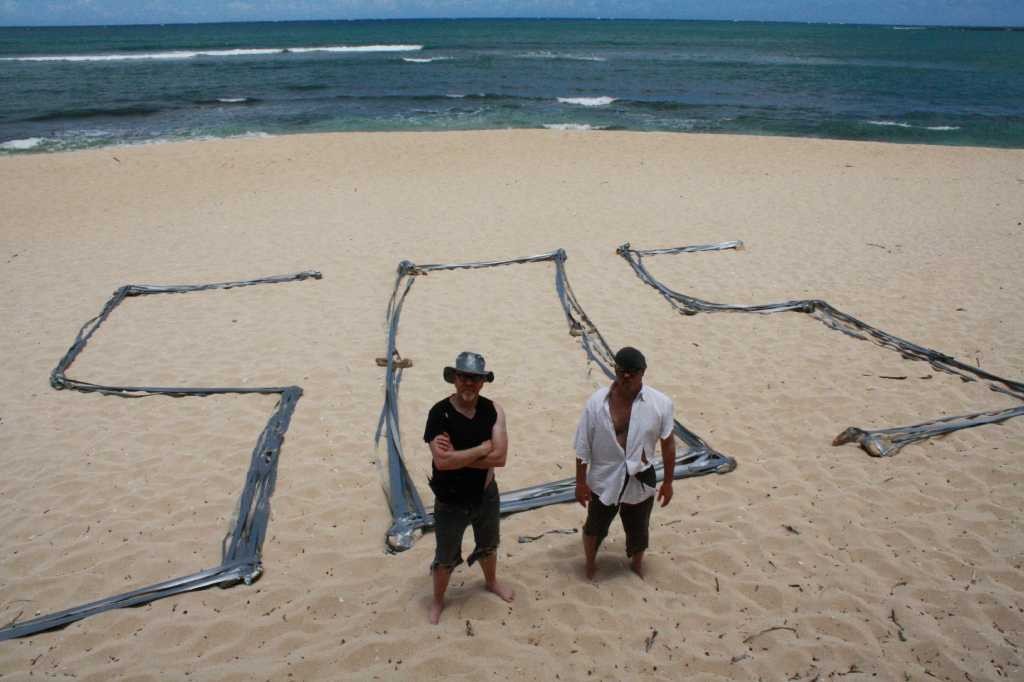 Episode Duct Tape Castaway/Island. Host Adam Savage and Jamie Hyneman on beach with duct tape 'SOS.'